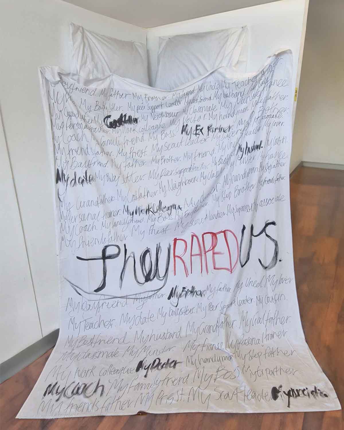 'They Raped Us', 2025. Bedsheet, pillows, black and red ink